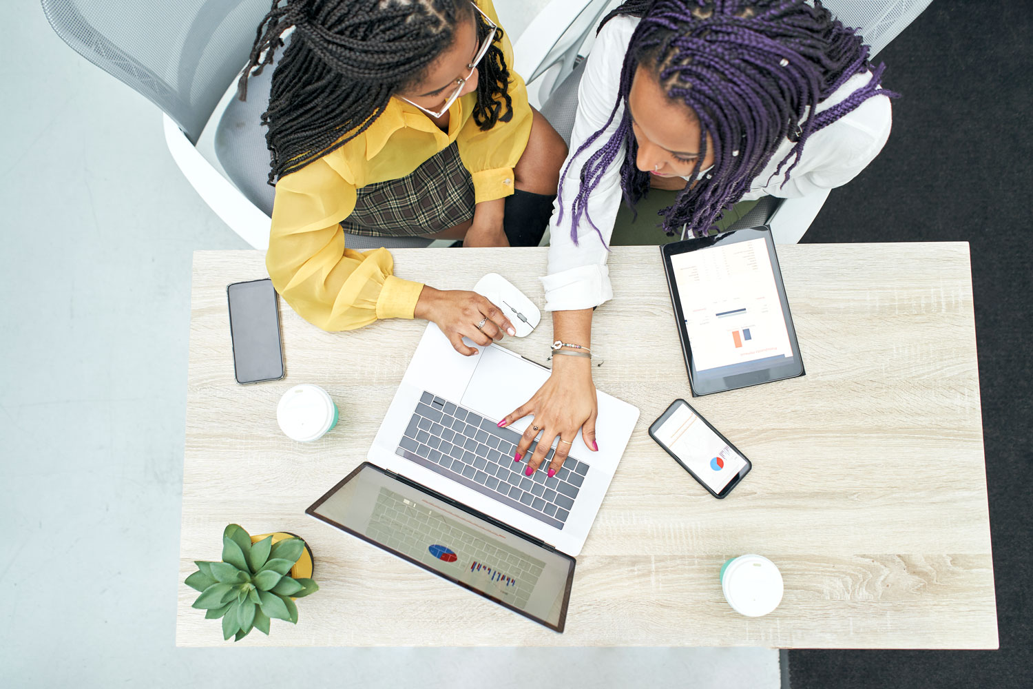 Two women sitting at a table with laptops.